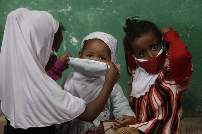 Una mujer le pone la mascarilla a un par de niños.