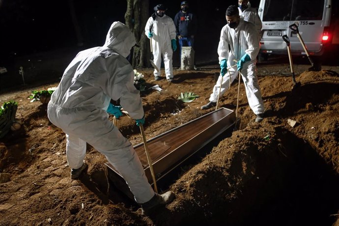 02 April 2021, Brazil, Sao Paulo: Employees of the Vila Formosa cemetery, the largest in Latin America, carry a coffin to bury a person who died of coronavirus (Covid-19). Due to the high number of deaths, the employees also work during the night. Photo