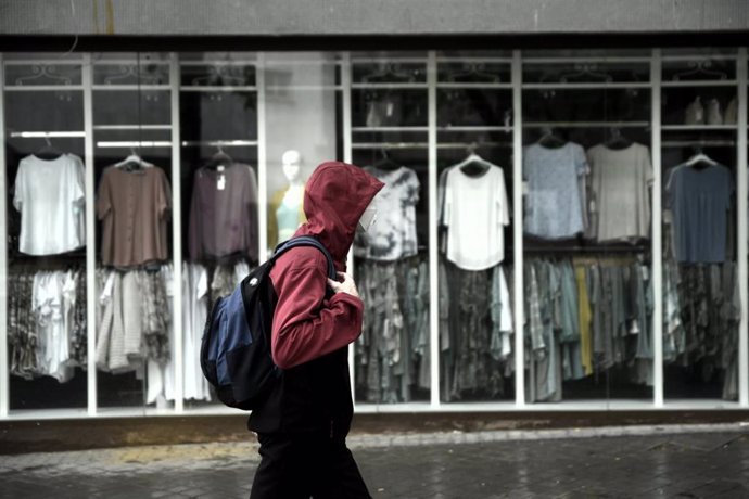 Archivo - Un hombre pasea frente a una tienda de ropa en un día de lluvia y bajada de temperaturas (imagen de archivo).