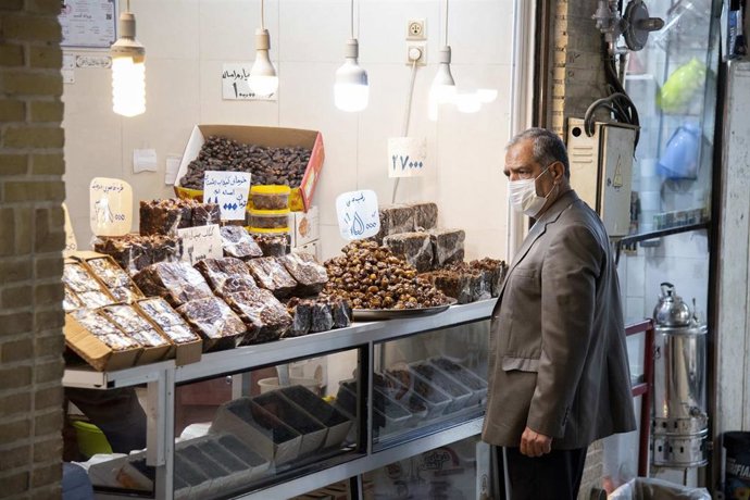Un hombre con mascarilla ante una tienda en Qom, Irán