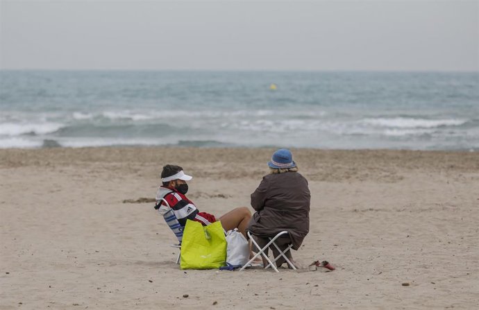 Dos personas sentadas con mascarilla en la playa la Malvarrosa en Valncia