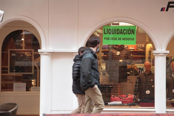 Archivo - Dos personas pasan por delante de un establecimiento abierto donde se puede leer "Liquidación por cese de negocio".