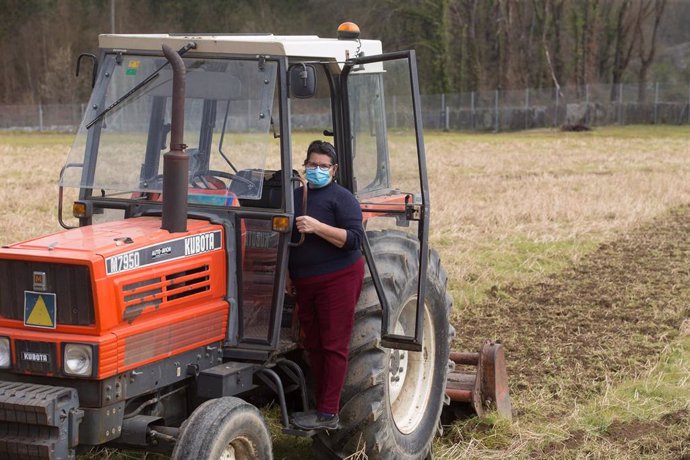 Una mujer con marcarilla en su tractor para plantar patatas 