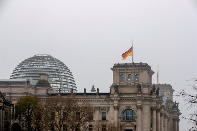 18 April 2021, Berlin: The German flag on top of the Reichstag building flies at half-mast during a commemorative event for all those who have died since the outbreak of the coronavirus (COVID-19). Photo: Christoph Soeder/dpa