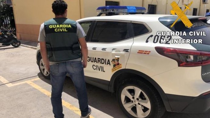Archivo - Un agente de la Guardia Civil frente a un vehículo policial