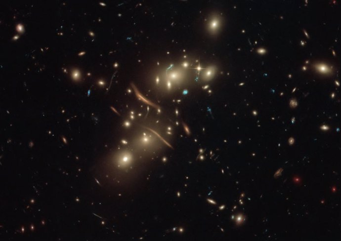 La luz de las galaxias de fondo resulta deformada por el efecto de lente gravitacional de un cúmulo galáctico en primer plano