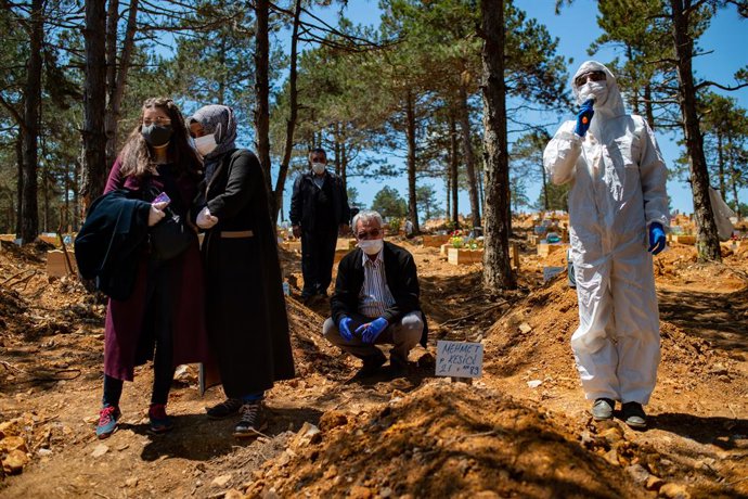 Archivo - 30 May 2020, Turkey, Istanbul: People mourn and pray in a cemetery over the grave of a relative who died of Coronavirus (COVID-19), next to a morgue worker wearing a protective suit. Photo: Yasin Akgul/dpa