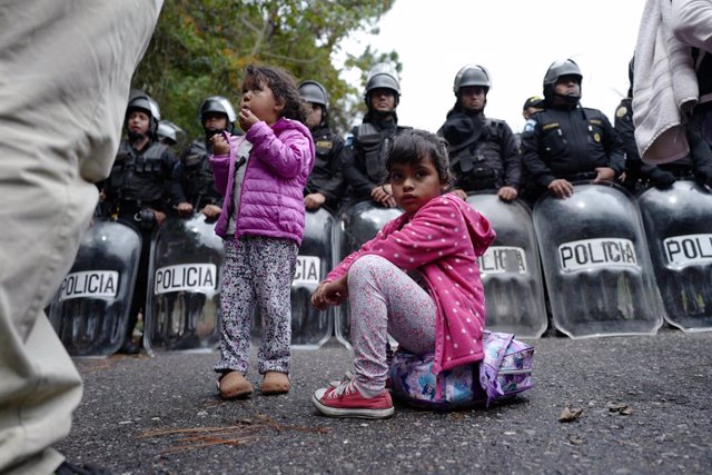 Archivo - 16 January 2019, Guatemala, Aguas Calientes: A migrant child sits on his backpack in front of a number of police officers at the Aguas Calientes border crossing between Honduras and Guatemala, as she takes her way to the north, plans to immigr