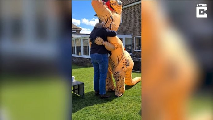 Una madre y su hija se visten con disfraces de dinosaurio para abrazar a sus abuelos