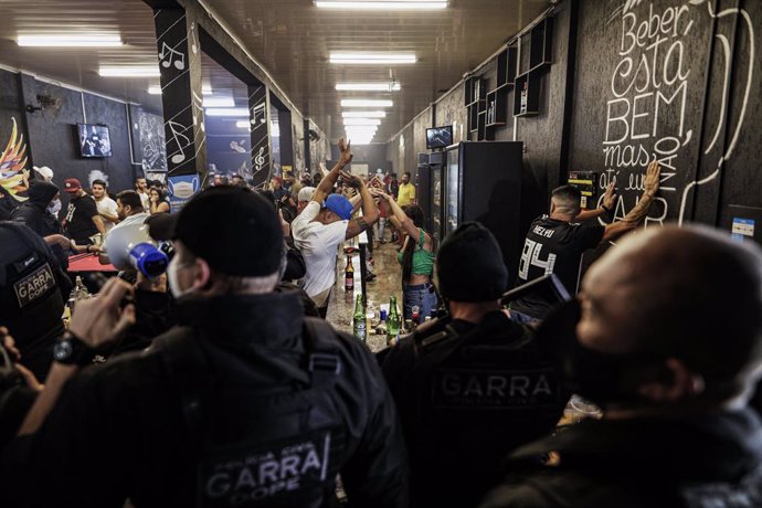 21 April 2021, Brazil, Jandira: Bar-goers stand with their heads above their heads during a police raid to break up a social gathering amid the coronavirus pandemic. Photo: Marcelo Chello/ZUMA Wire/dpa