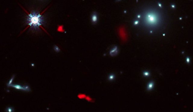 Imagen del cúmulo de galaxias RXCJ0600-2007 tomada por el telescopio Hubble de la NASA/ESA combinada con imágenes de lente gravitacional de la lejana galaxia RXCJ0600-z6, situada a 12.400 millones de años luz de distancia, obtenidas con ALMA (en ropjo)