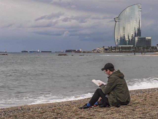 A man is seen sitting at barceloneta beach while reading a book instead of bathing