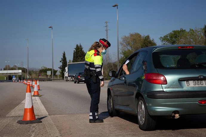 Archivo - Una agente de los Mossos d'Esquadra protegida con una mascarilla en un control en el peaje de La Roca del Valls pide a un conductor un justificante.