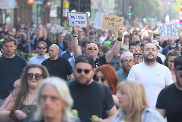 24 April 2021, United Kingdom, London: A protester holds two placards reading "Question everything" and "Wake up world". Thousands marched on London's Oxford Street as part of the Unite For Freedom protest against the nationwide Corona restrictions. Pro