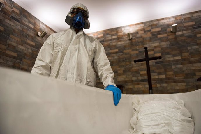 12 April 2021, Chile, Temuco: A staff member of the Lar de Cristo Funeral Home is seen dressed in full protective suit as he stands next to a casket. The funeral home reported a 20 percent increase in funeral services in the wake of the Coronavirus pand