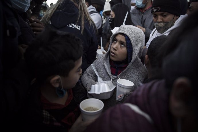 Archivo - 19 February 2021, Mexico, Tijuana: A migrant child receives a meal amid a crowd of awaiting asylum seekers at the El Chaparral between Mexico and the US. Starting from today, the new US administration under US President Joe Biden will graduall
