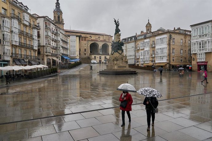 Archivo - Dos personas se refugian con un paraguas de la lluvia en Vitoria