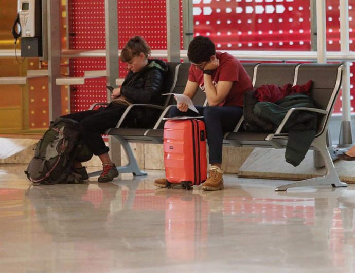 Archivo - Dos personas con su equipaje esperan su vuelo sentados en un banco en el Aeropuerto de Madrid-Barajas Adolfo Suárez, en Madrid a 21 de noviembre de 2019.