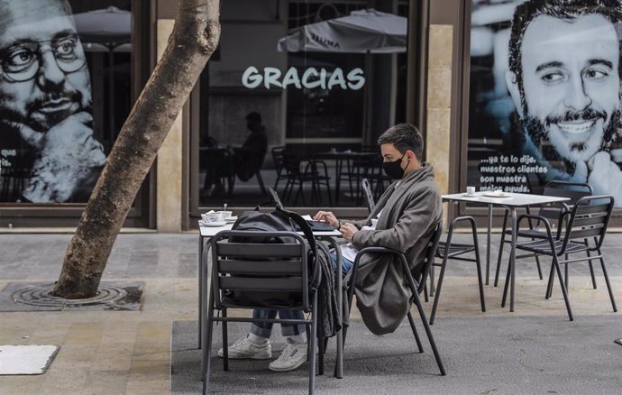 Archivo - Un joven trabaja con su ordenador portátil en una terraza el primer día de la apertura de la hostelería en Valencia, 