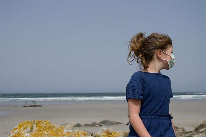 Una niña lleva una mascarilla en la playa