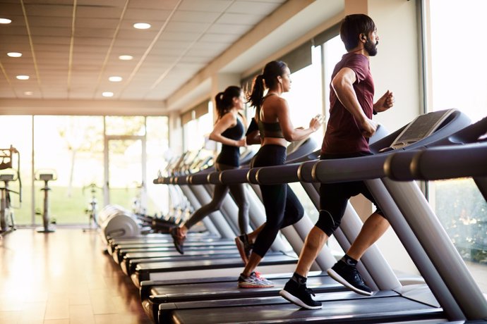 Archivo - Vista de una fila de cintas de correr en un gimnasio con gente.