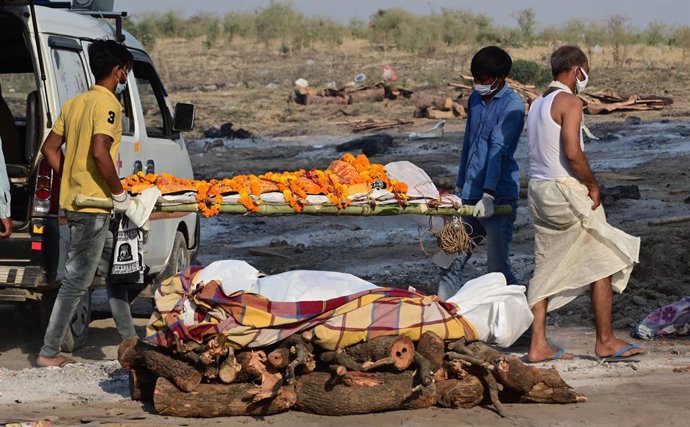 27 April 2021, India, Prayagraj: Family members and paramedics carry the bodies of victims who died who died of Covid-19 disease to the cremation sites at Phaphamau Ghat. India hit record numbers of Covid-19 infections worldwide for the sixth day runnin