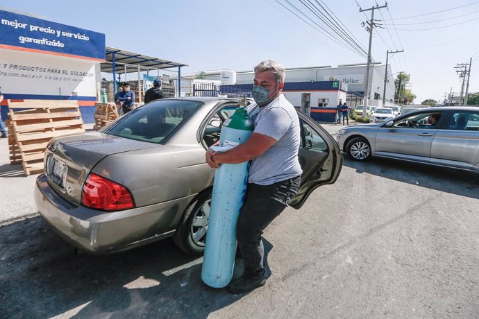 Archivo - 21 January 2021, Mexico, Queretaro: A man carries an oxygen cylinder as people line up to buy oxygen for their relatives infected with the coronavirus disease (COVID-19). Mexico faces a shortage of oxygen tanks and a fourfold rise in prices as