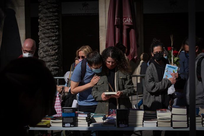 Dos jóvenes miran un libro, en la Plaza Real de Barcelona en el día de Sant Jordi, a 23 de abril de 2021, en Barcelona, Catalunya, (España)
