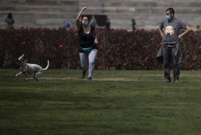 Un hombre y una mujer, con mascarilla, juegan con un perro en el Parque del Manzanares, el día en que entra en vigor el uso obligatorio de mascarilla incluso con distancia de seguridad, en Madrid (España), a 31 de marzo de 2021. Hoy entra en vigor el Pr