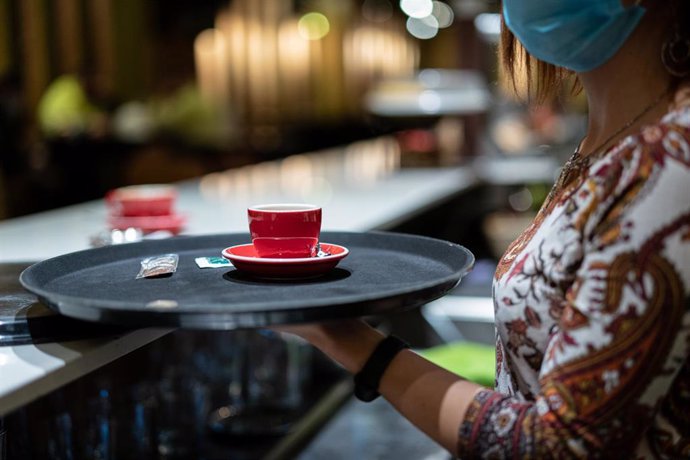 Archivo - Una trabajadora lleva un café a una mesa en una cafetería.