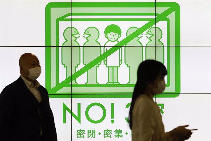 23 April 2021, Japan, Tokyo: Pedestrians wearing face masks walk past a screen showing measures to prevent the spreading of the new coronavirus after the Japanese Prime Minister Yoshihide Suga declared a state of emergency for Tokyo and the prefectures 