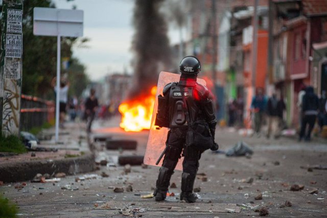 30 April 2021, Colombia, Bogota: A riot police officer stands behind burning tiers during clashes at a protest against the tax reform bill proposed by the government. Photo: Chepa Beltran/VW Pics via ZUMA Wire/dpa