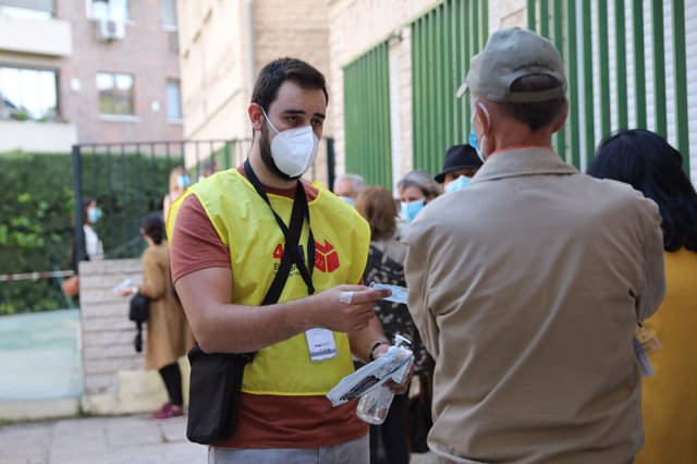 Un trabajador de las votaciones ofrece mascarillas y gel hidroalcohólico a las personas que hacen cola para votar en el Colegio Joaquín Turina, a 4 de mayo de 2021, en Madrid (España). 