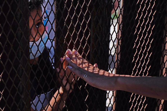 30 April 2021, US, Nogales: A supporter touches the hand of a young asylum-seeking migrant from behind the fence at border wall separating the United States and Mexico. Photo: Christopher Brown/ZUMA Wire/dpa