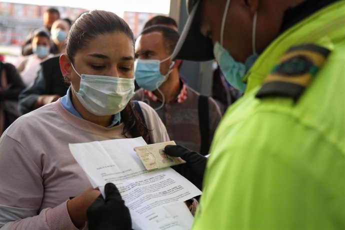 Un policía registra los documentos de una ciudadana para permitirle el acceso a un comercio en etapa de restricciones por coronavirus en Bogotá.  