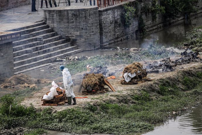 03 May 2021, Nepal, Kathmandu: A worker wearing personal protective equipment (PPE) cremates the body of a COVID-19 victim on the bank of Bagmati River. The Nepalese government banned all domestic and international flights until 14 May in an attempt to 
