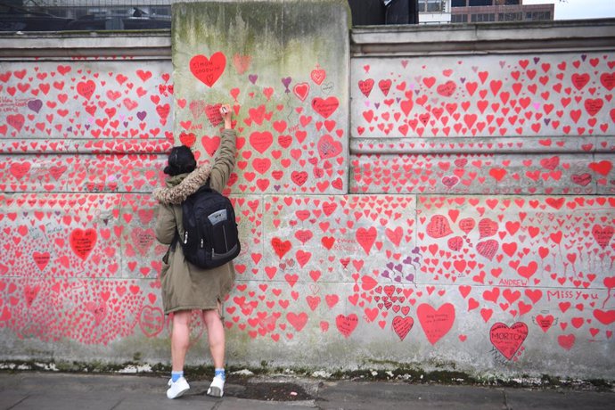08 April 2021, United Kingdom, London: A woman draws a heart on the National Covid Memorial Wall which commemorates people who died in the UK from coronavirus. Photo: Victoria Jones/PA Wire/dpa