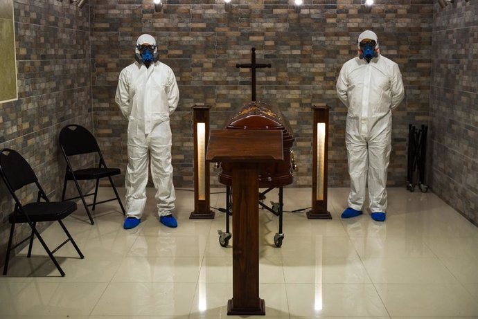 12 April 2021, Chile, Temuco: Lar de Cristo Funeral Home staff are seen dressed in full protective suits as they stand next to a casket. The funeral home reported a 20 percent increase in funeral services in the wake of the Coronavirus pandemic. Photo: 