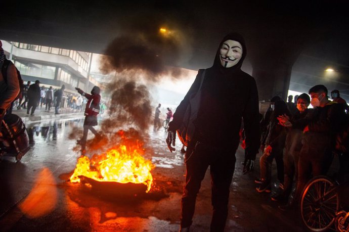 28 April 2021, Colombia, Bogota: Aprotester wearing a Guy Fawkes mask stands in front of burning tires during clashes at a protest against the government's tax reform bill. Photo: Chepa Beltran/LongVisual via ZUMA Wire/dpa
