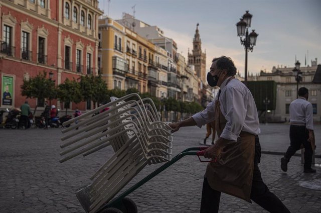 Archivo - Un camarero recoge el mobiliario de la terraza de un bar, foto de archivo   