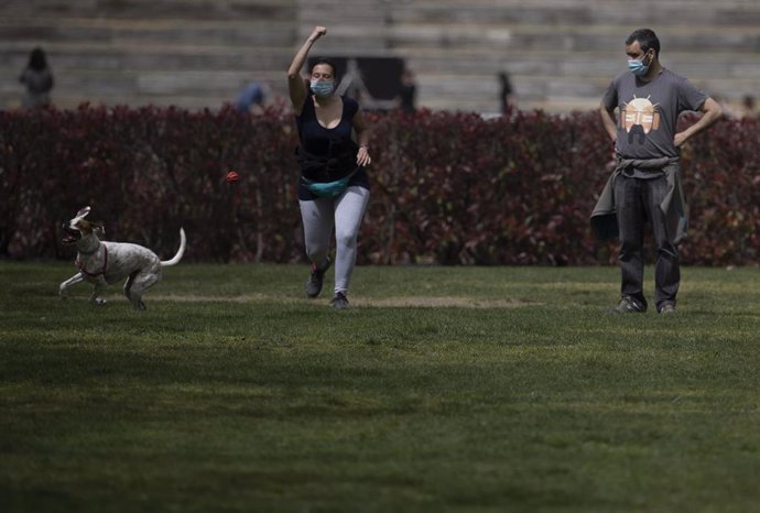 Archivo - Un hombre y una mujer, con mascarilla, juegan con un perro en el Parque del Manzanares, el día en que entra en vigor el uso obligatorio de mascarilla incluso con distancia de seguridad, en Madrid (España), a 31 de marzo de 2021. Hoy entra en v