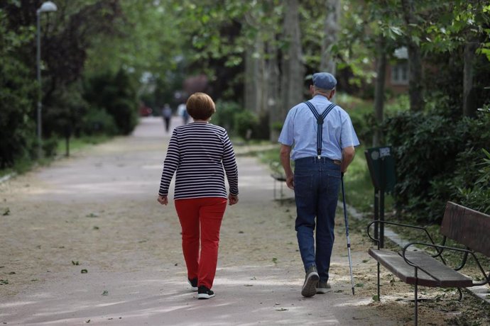 Archivo - Una mujer y un hombre de edad avanzada con bastón caminan por un parque de Madrid.
