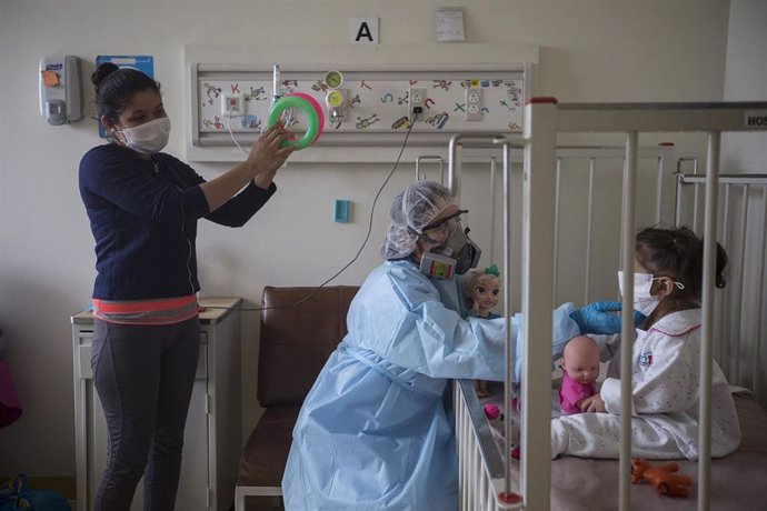 Archivo - Una mujer y una enfermera entretienen a una niña con coronavirus en el Hospital Infantil San Borja, en Lima.