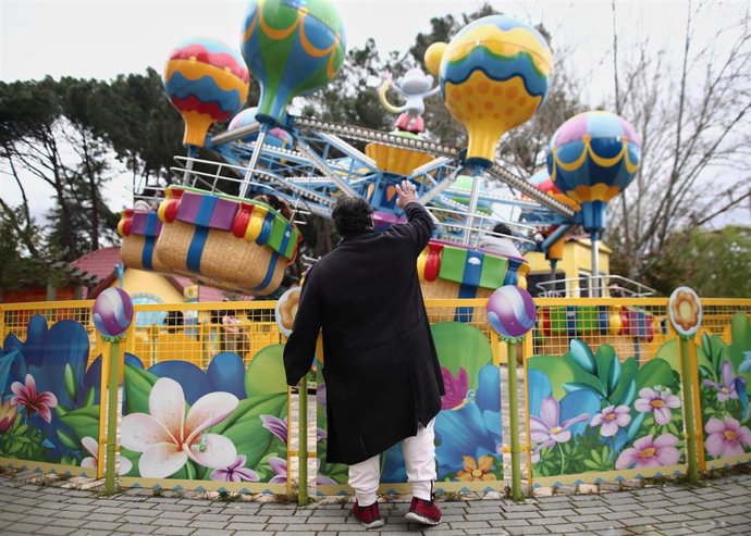 Archivo - Un hombre saluda a un niño que está subido en una atracción infantil del Parque de Atracciones.