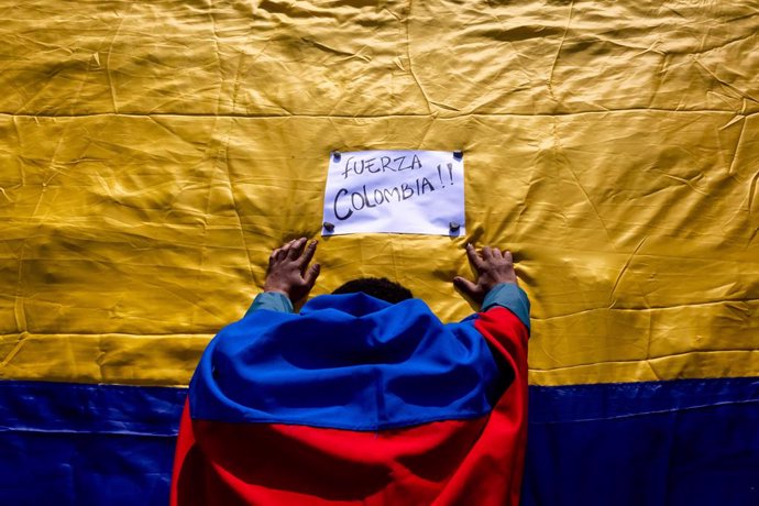 07 May 2021, Chile, Puerto Montt: A protester stands in front of aplacard reading "Be strong, Colombia" placed on a Colombian flag during a rally to support the Colombina protestors. Photo: Felipe Constanzo/Agencia Uno/dpa