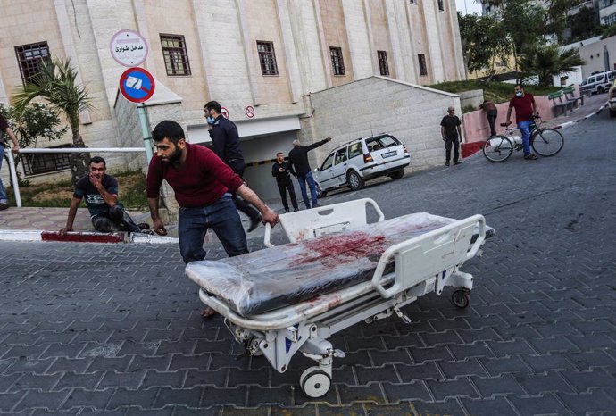 GRAPHICS - 10 May 2021, Palestinian Territories, Gaza City: APalestinian man wheels a hospital bed stained with blood at a hospital in the northern Gaza Strip, where those who were wounded or killed amid the escalating Israeli-Palestinian violence are 
