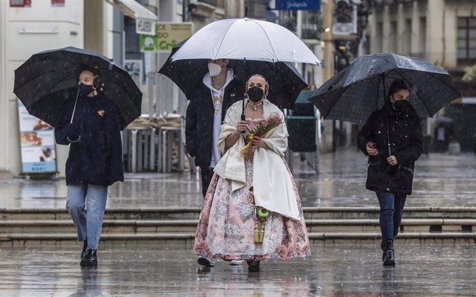 Una fallera se dirige a la Basílica de Valncia con un paraguas y un ramo de flores para la Virgen de los Desamparados