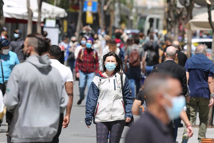 Varias personas caminan por el centro de una ciudad llevando mascarilla.