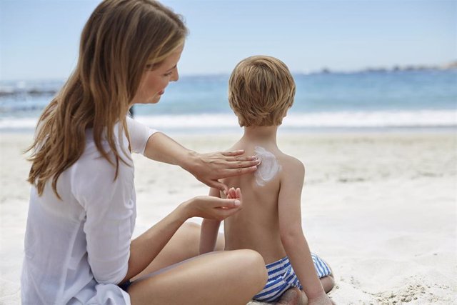 Madre poniendo crema de fotoprotección solar a su hijo en la playa.
