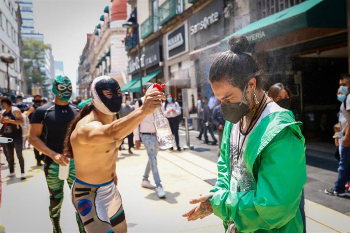 Un luchador mexicano desinfecta a un ciudadano en un evento sobre el uso de mascarilla y cumplimiento de medidas en Ciudad de México.